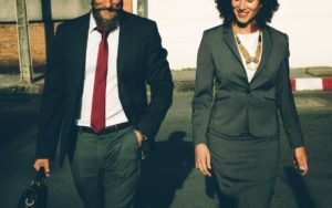 A man and a woman dressed in business wear walk down the street side by side