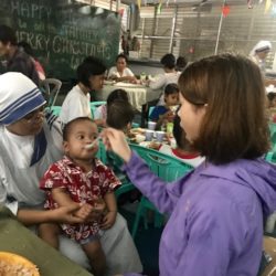 A young girl feeds a baby orphan being held by a nun in the Philippines