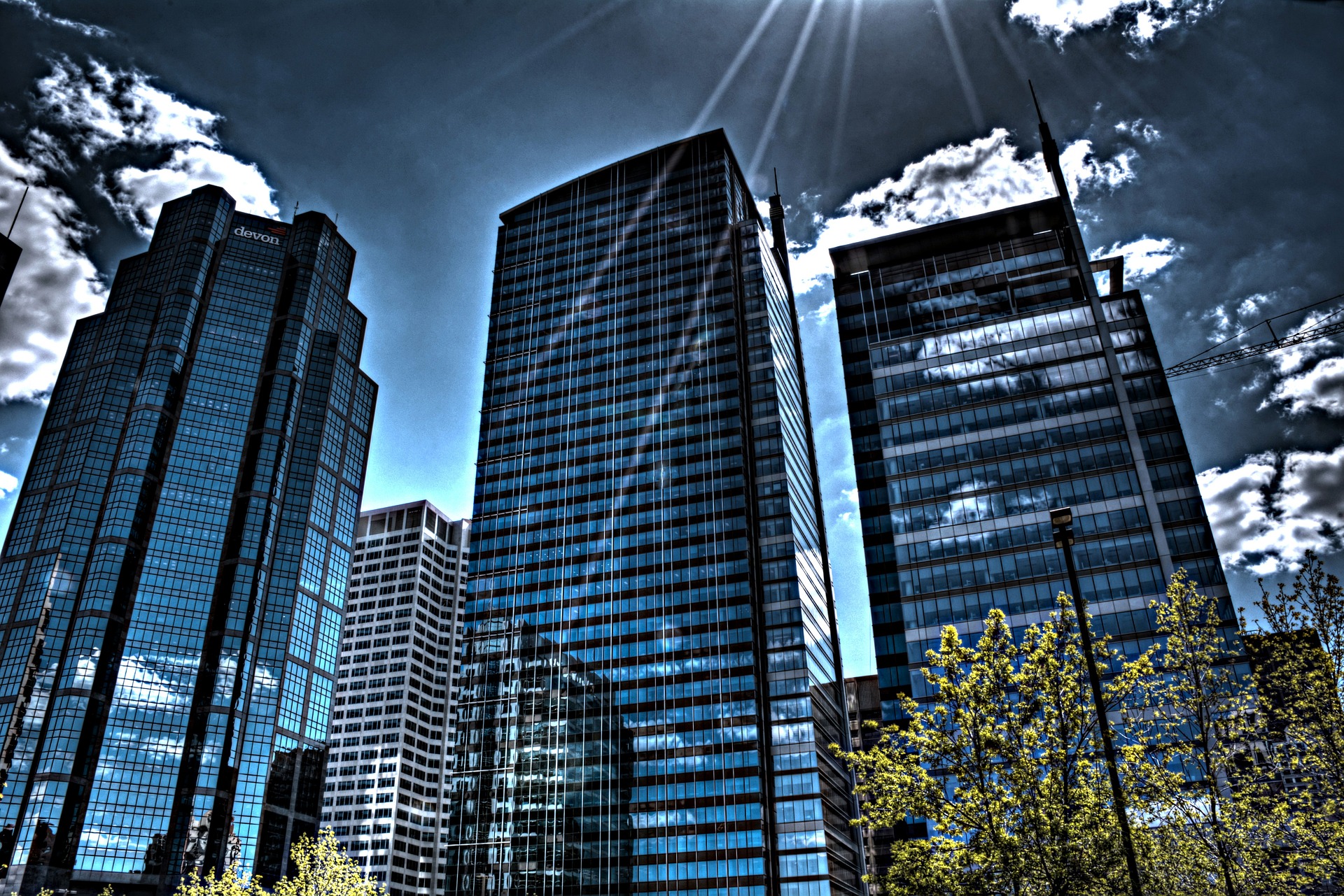 An image of tall blue skyscrapers in front of a blue sky with white fluffy clouds in Calgary, Alberta, Canada